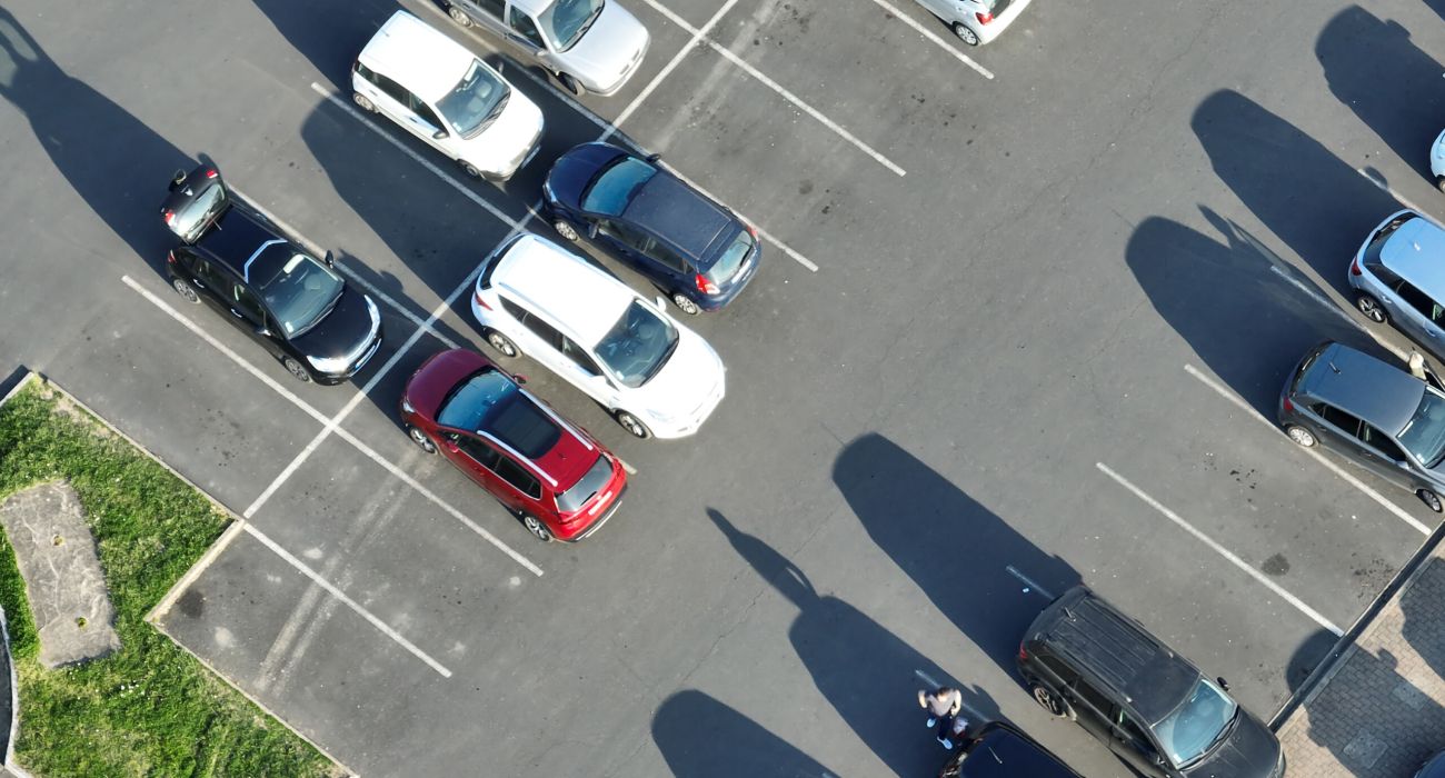 Aerial view of many colorful cars parked on parking lot with lines and markings for parking places and directions.